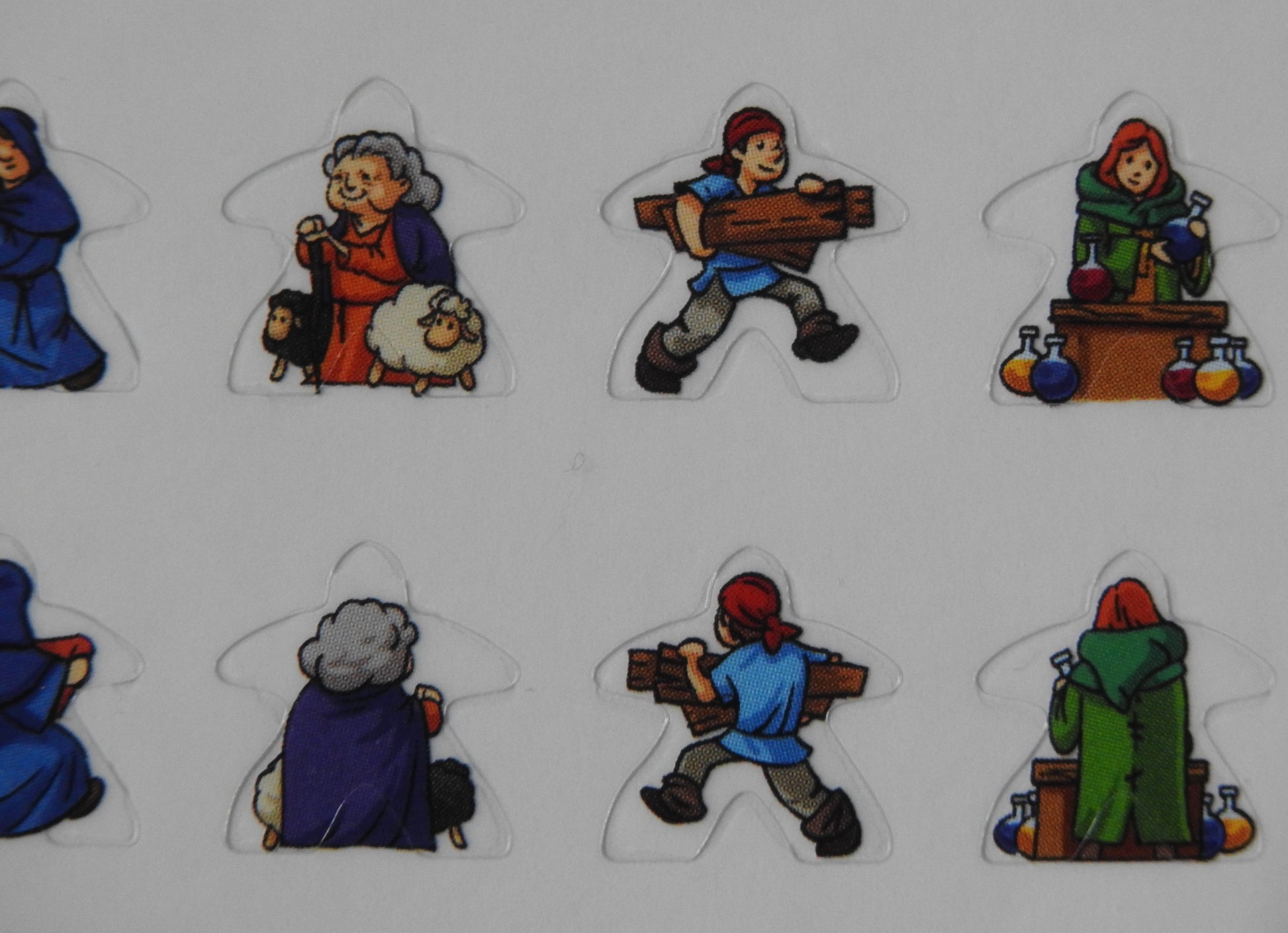 Close-up view of some of the meeple stickers, including a man gathering wood and a lady with various potions around her.