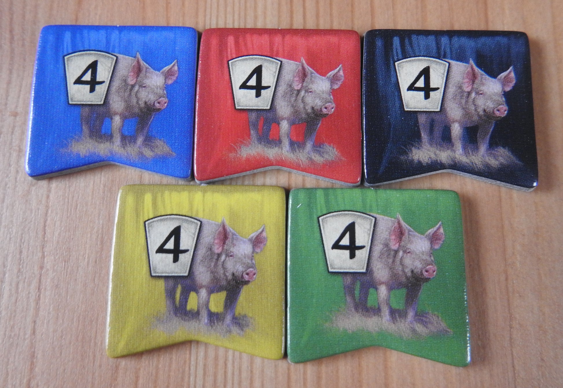 Close-up view of the 5 pig tokens in the different colours - blue, red, black, yellow and green.