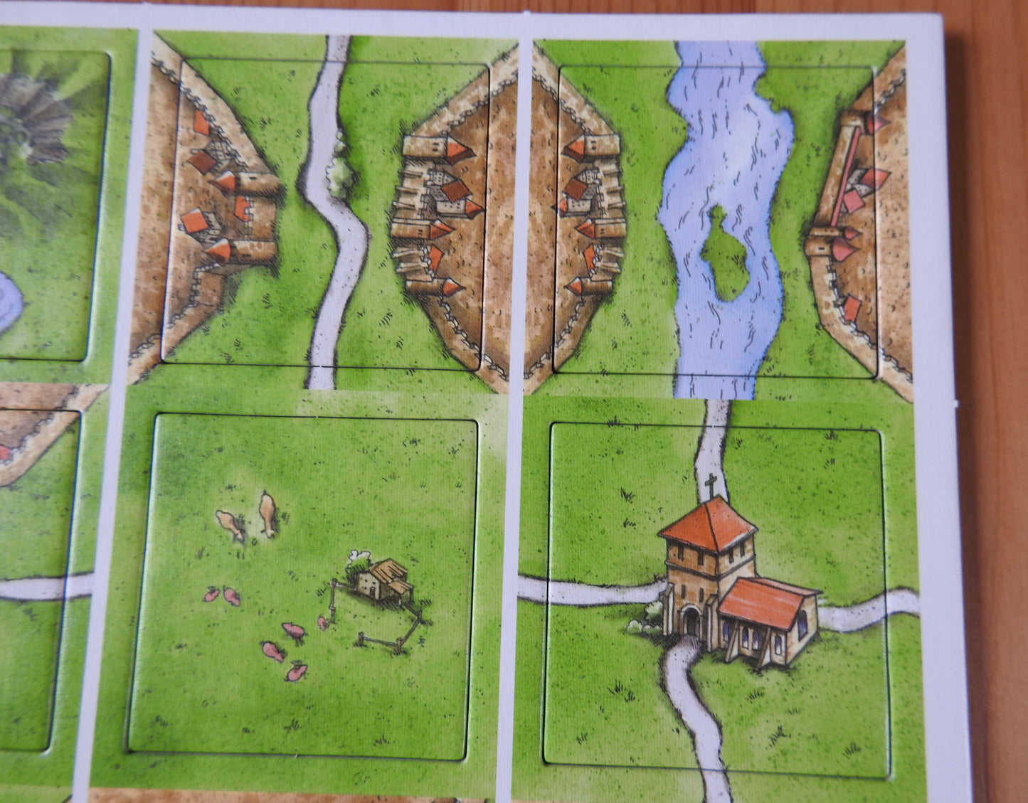 Close-up of 4 of the included tiles, featuring a monastery, a river and a pig farm.