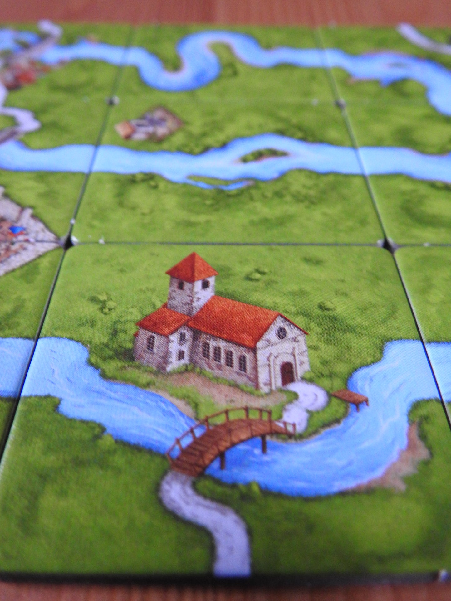 A close-up of an old monastery next to a bridge on the river in this River I mini expansion for Carcassonne.