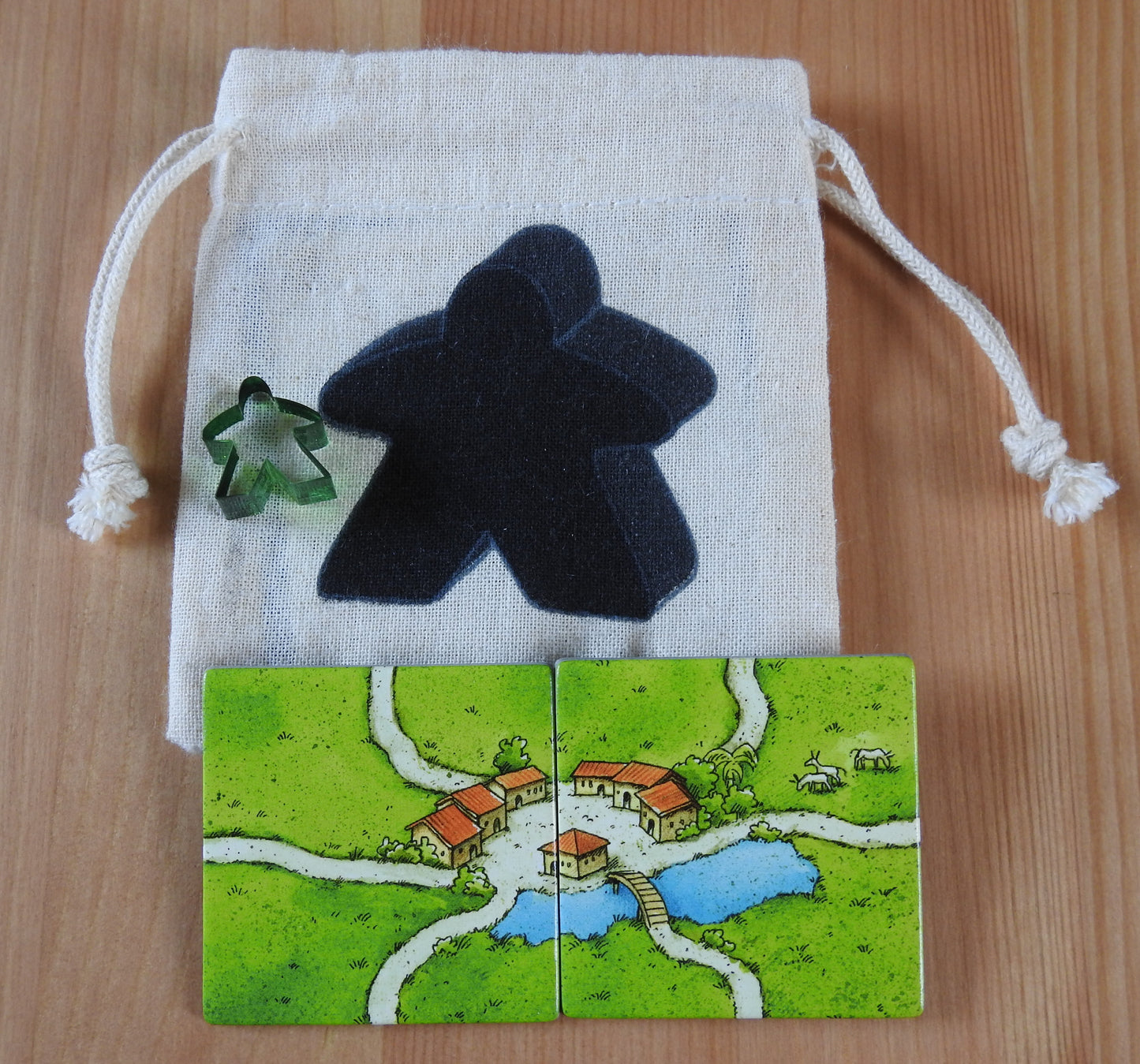 Close-up of the black meeple bag, green meeple teacher and 2 tiles.