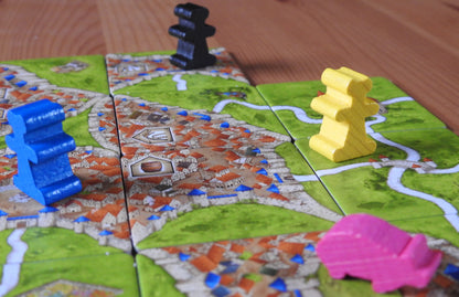Close-up showing some of the wooden trader and pig meeple figures on the landscape tiles included in this Carcassonne Traders & Builders Unboxed expansion.