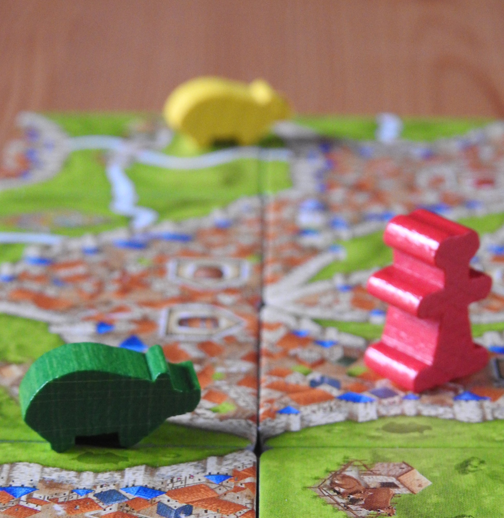 View showing some more of the wooden pig and traders figures arranged on landscape tile that are part of this Carcassonne Traders & Builders Unboxed expansion.